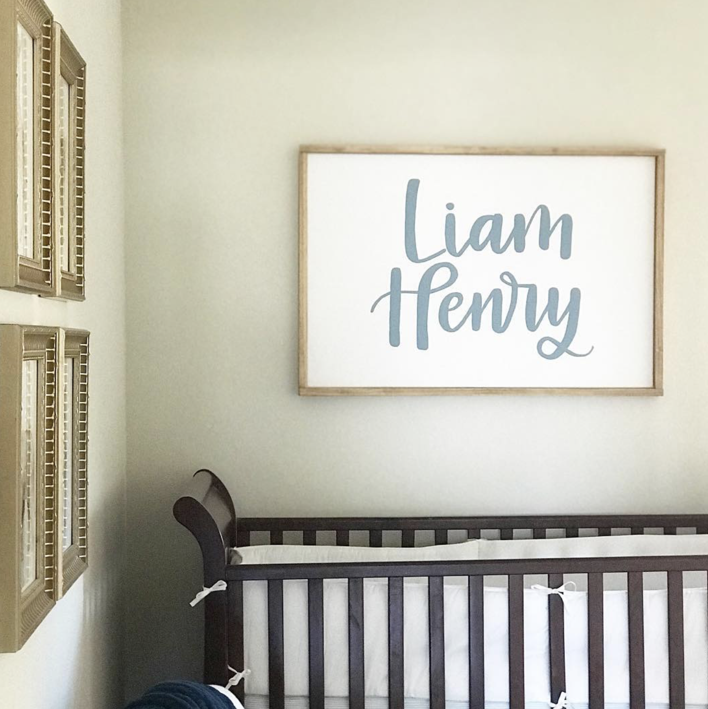 Nursery room with a dark wood crib and a large wall sign with the name "Liam Henry" in blue cursive lettering.