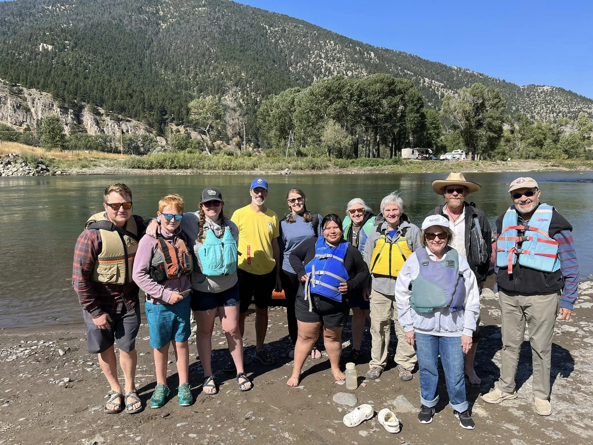 People wearing life jackets gather beside a river.