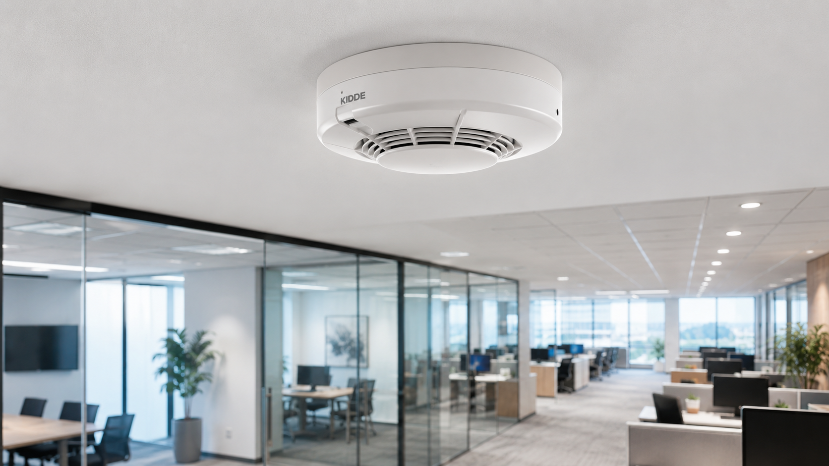 Ceiling smoke detector in a modern office space with glass walls and desks.
