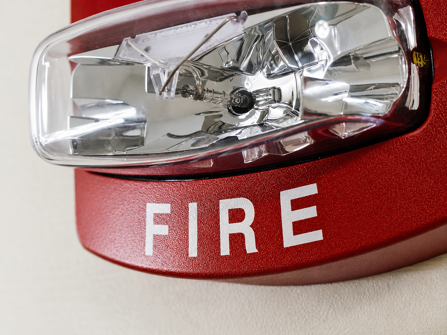 Close-up of a red fire alarm with a clear cover and a black button inside, placed on a beige surface.