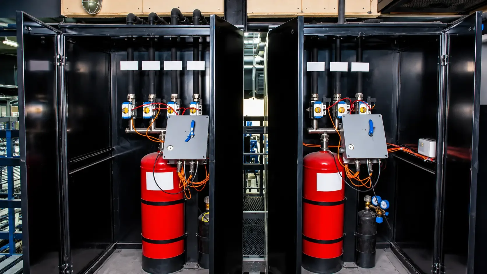 A fire suppression system cabinet with two fire extinguishers, gauges, piping, and electrical components inside a black metal enclosure