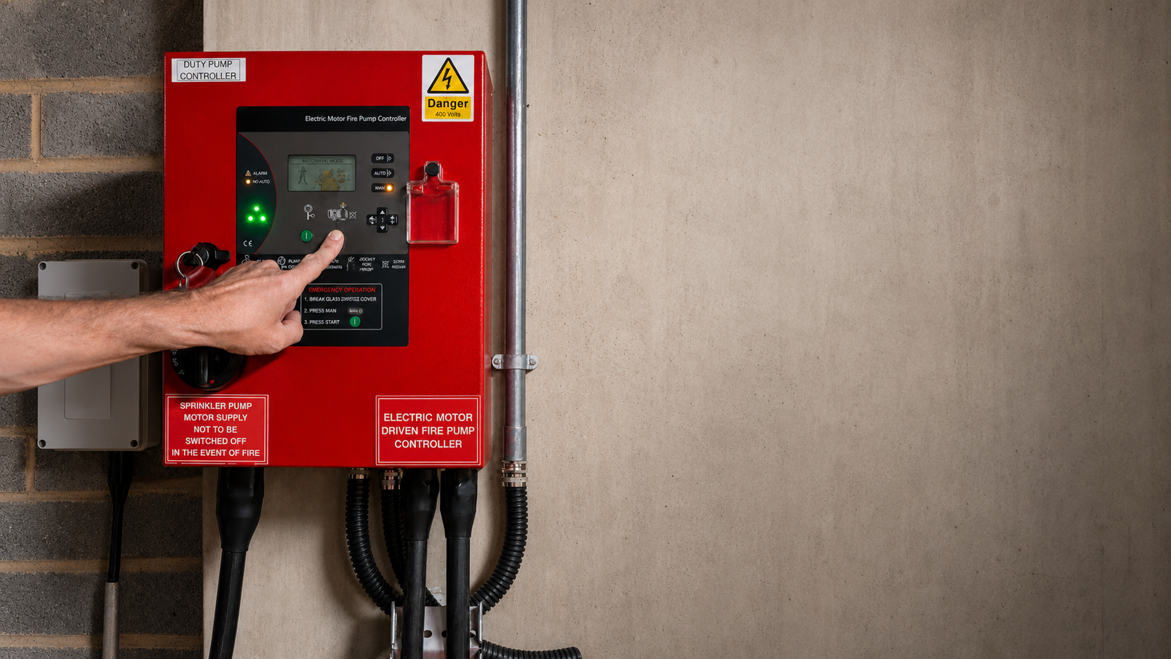 Person pressing a button on a red fire pump controller panel mounted on a wall.