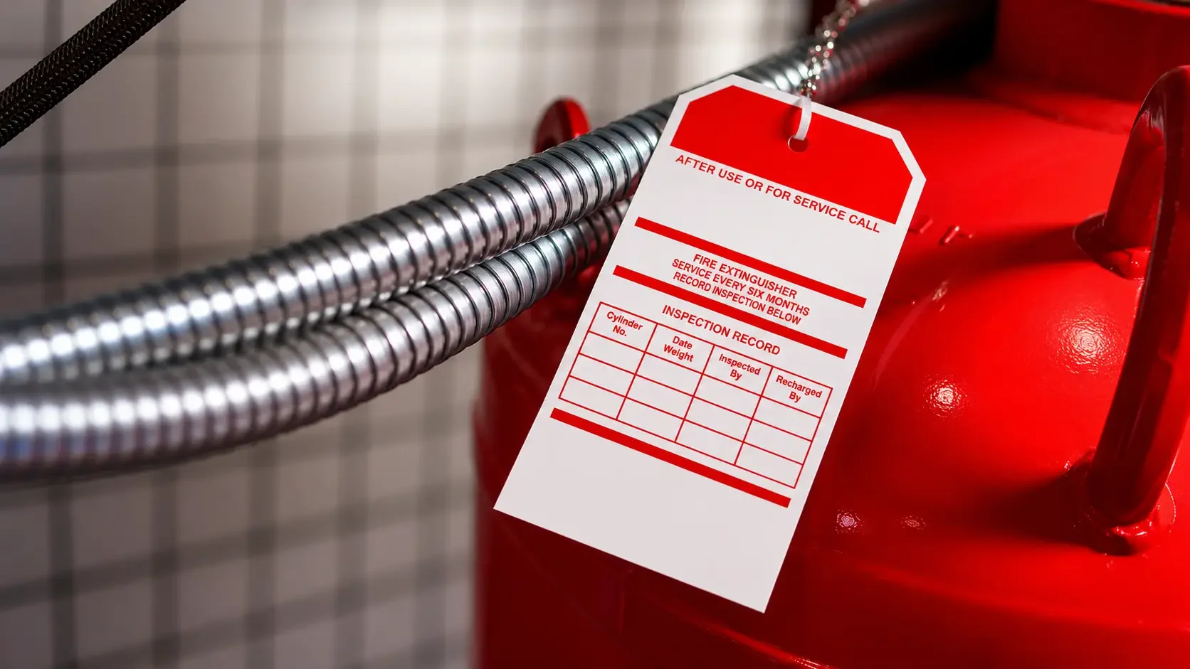 A red fire extinguisher with a white inspection tag hanging from a nearby pipe.