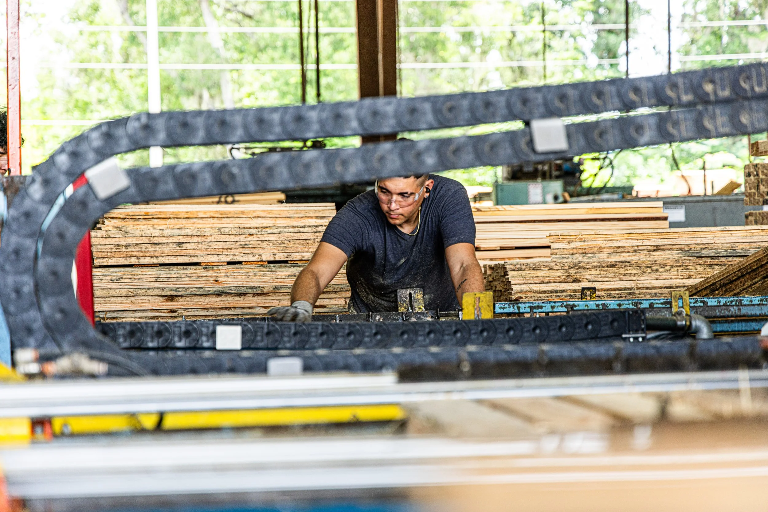A man working in a woodworking shop, surrounded by stacks of lumber and industrial equipment.
