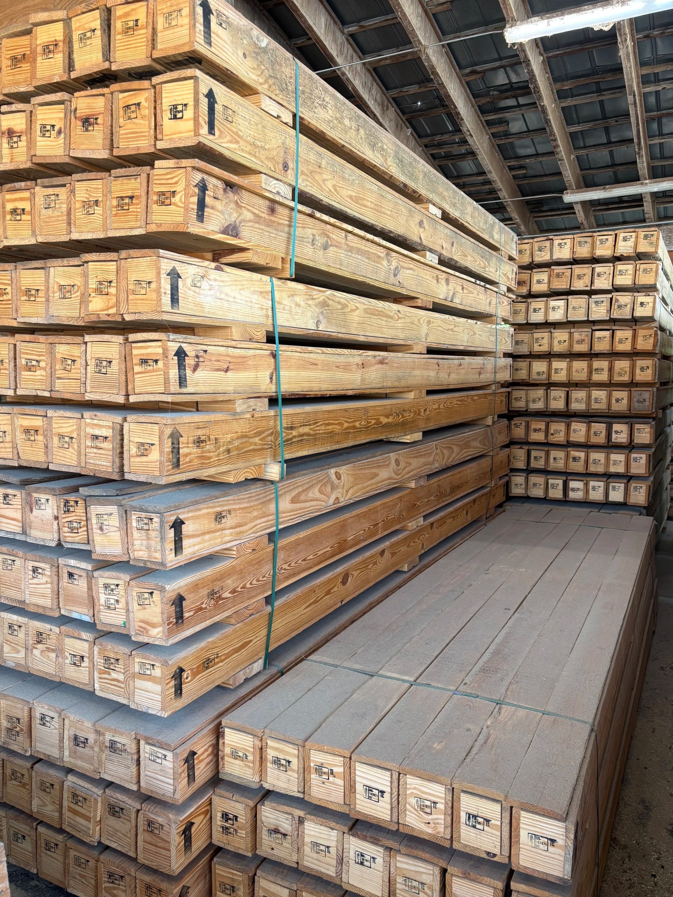 Stacks of wooden beams and planks stored on shelves in a warehouse, with some beams marked with black arrows and labels.