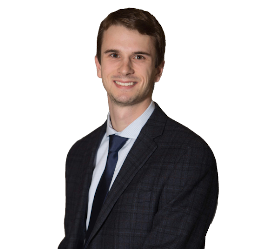 Portrait of a young man in a dark suit and blue tie, smiling against a white background.