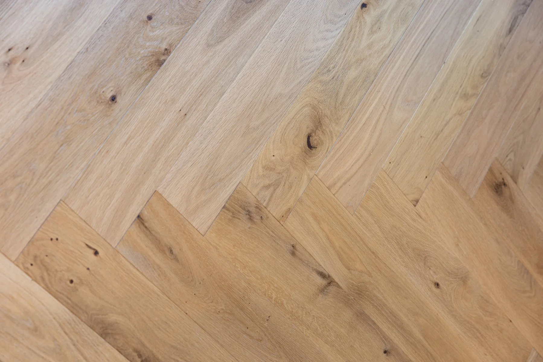 Close-up of a wooden parquet floor with a herringbone pattern, showing natural wood grain and knots.