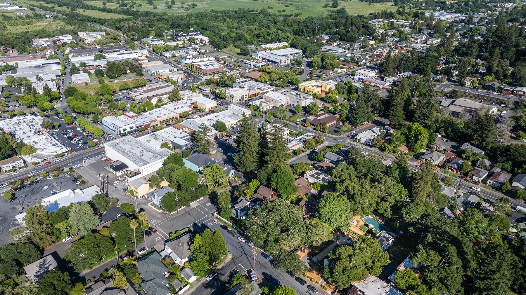 An aerial view of a small town with a mix of commercial and residential buildings surrounded by trees and greenery.