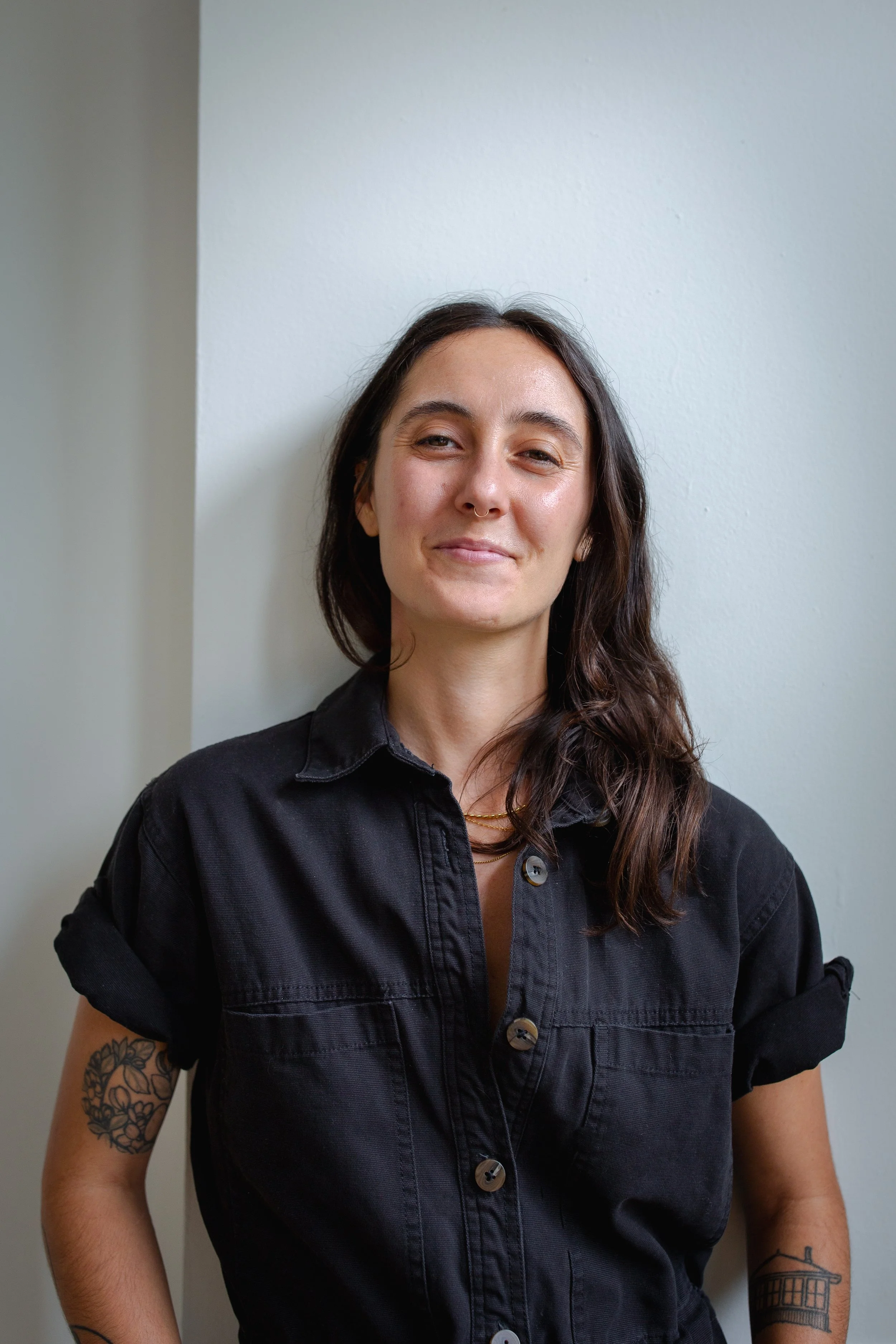 Kate leans against a wall wearing a black denim shirt.
