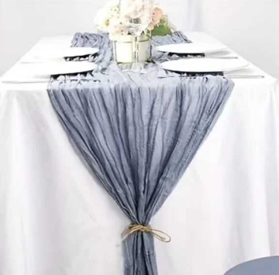Table élégante avec une nappe blanche, une bande de tissu gris foncé tissé, et un centre de décoration avec des fleurs blanches et roses.