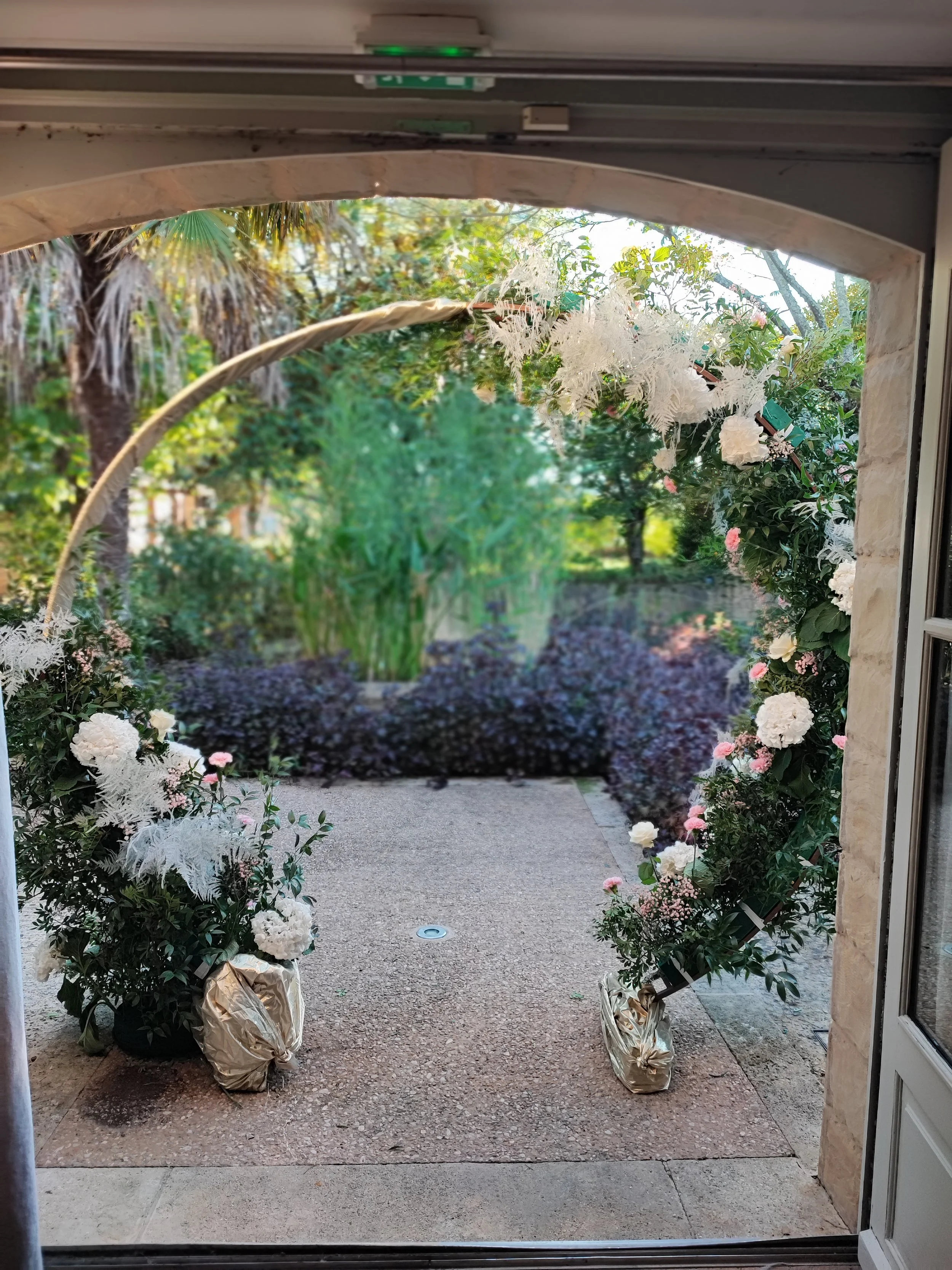 Deux arrangements floraux avec des plantes vertes et des fleurs blanches et roses, placés de chaque côté d'une porte d'entrée, pour une décoration de mariage ou d'événement.