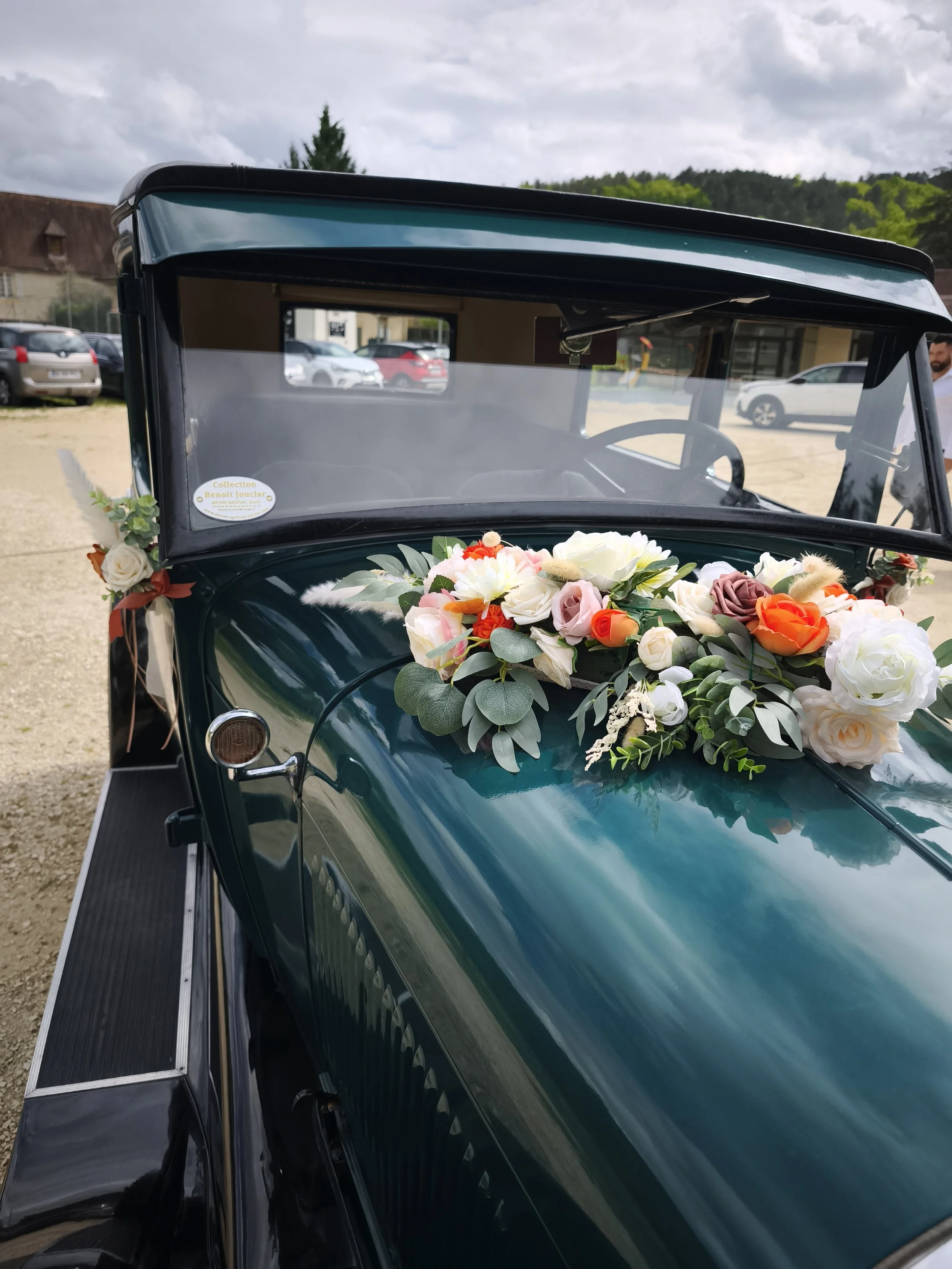 Une voiture ancienne verte décorée avec un bouquet de fleurs sur le capot, probablement pour un mariage.