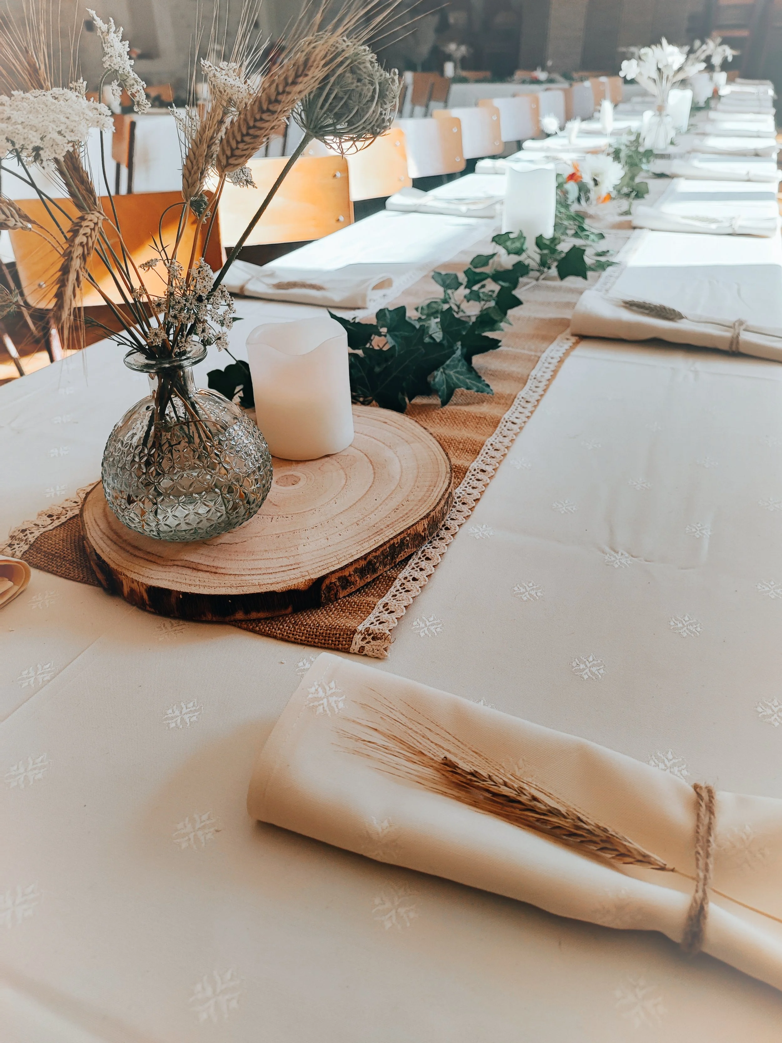 Une table décorée avec des fleurs séchées dans un vase, des bougies, une branche d'eucalyptus, et une nappe blanche festonnée, prête pour un événement spécial.