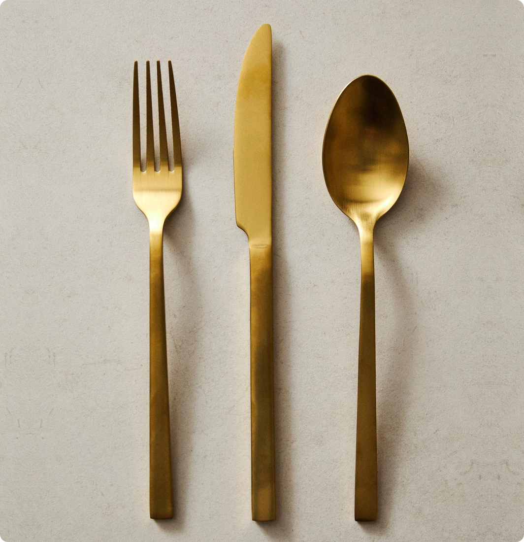 Une fourchette, un couteau et une cuillère en métal doré posés sur une surface claire.