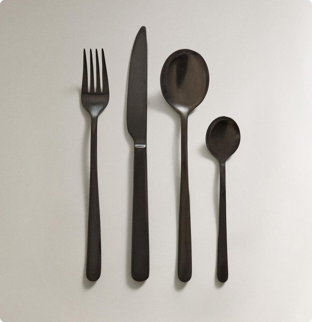 Four cuillères et couteau en métal noir disposés sur une surface blanche.