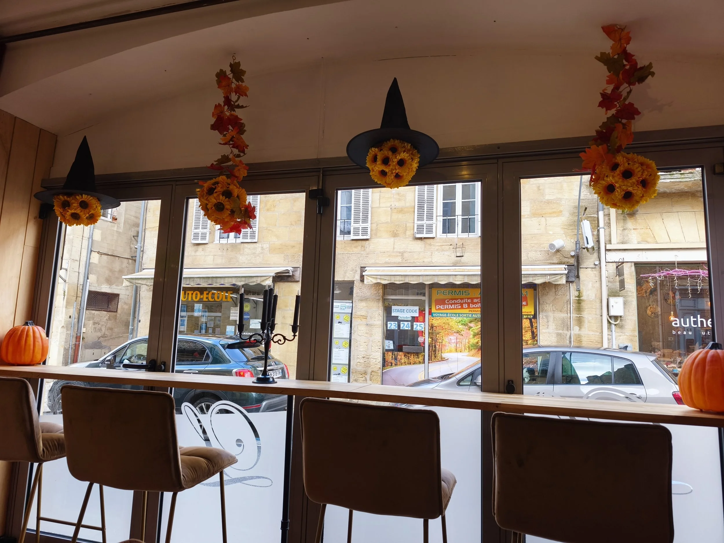 Décor d'automne avec des guirlandes de feuilles mortes et des citrouilles sur une table à l'intérieur, avec une vue sur la rue à travers une grande vitre.