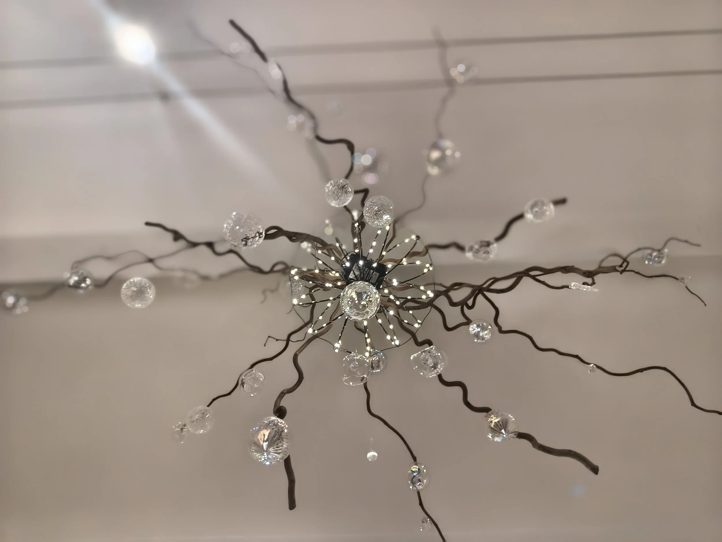 Un luminaire suspendu en forme de branche avec des décorations en forme de boules en plastique transparent avec des reflets lumineux.