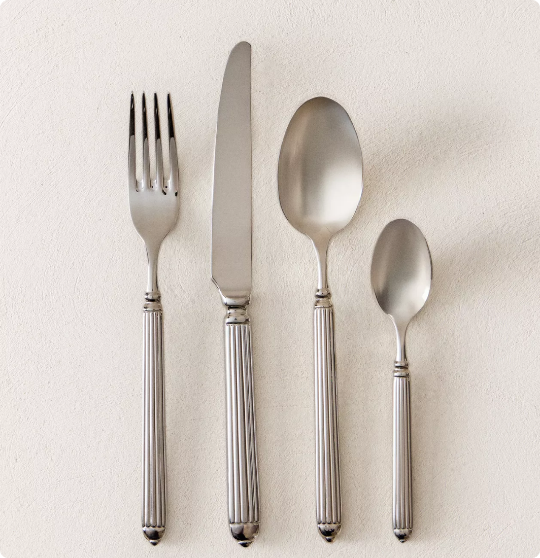 Une fourchette, un couteau, une grande cuillère et une petite cuillère en métal posés sur une surface claire.