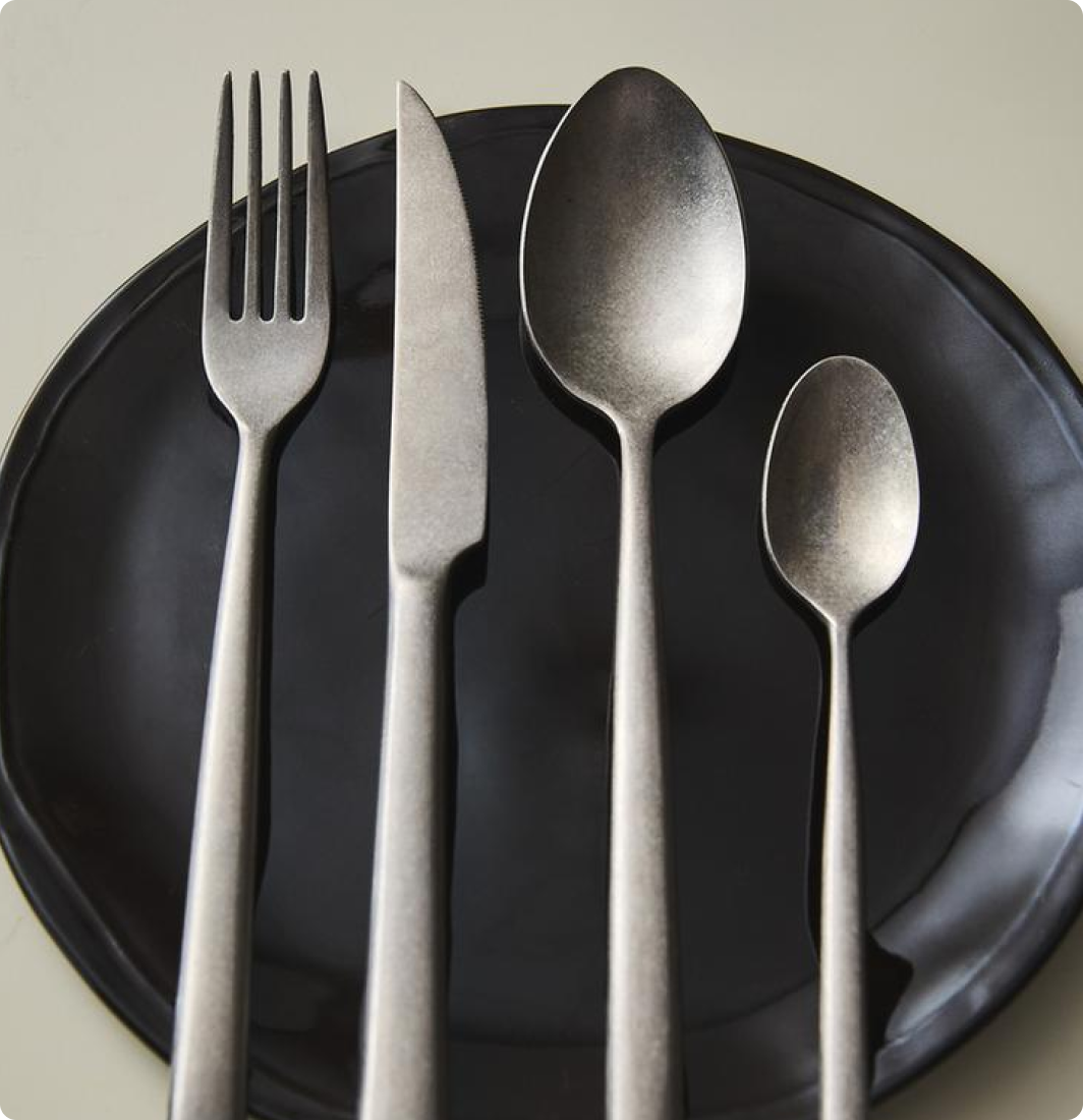 Une cuillère, une fourchette, un couteau, une grande cuillère et une petite cuillère en métal en ordre sur une assiette noire.