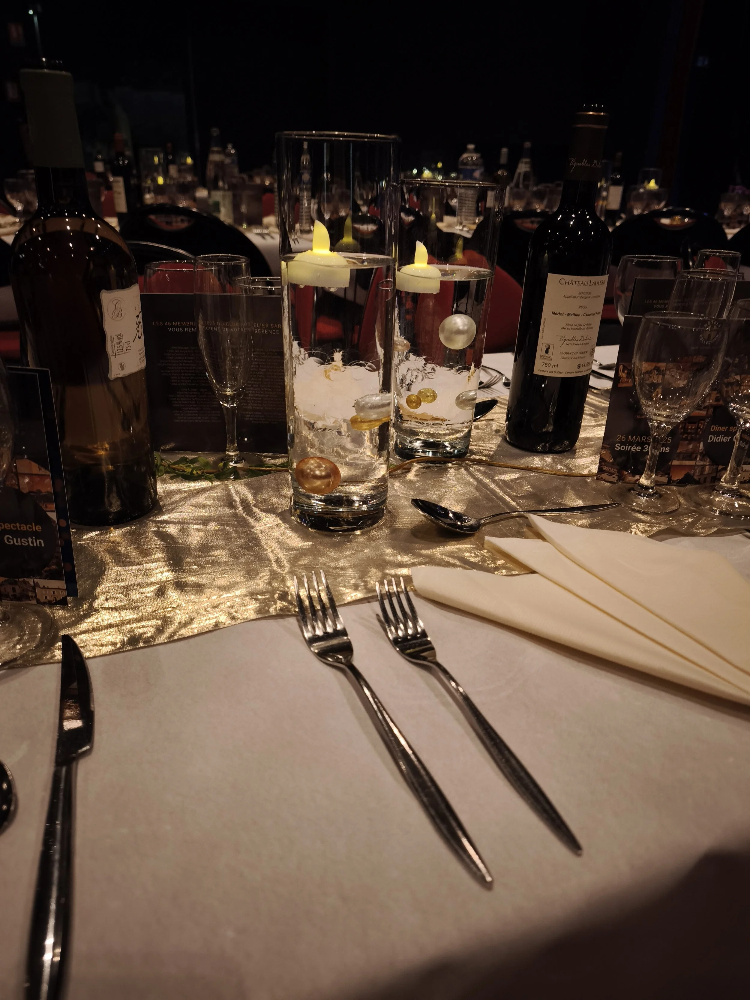 Une table de dîner élégante avec des verres, des bouteilles de vin, des bougies flottantes et des couverts, décorée pour un événement spécial