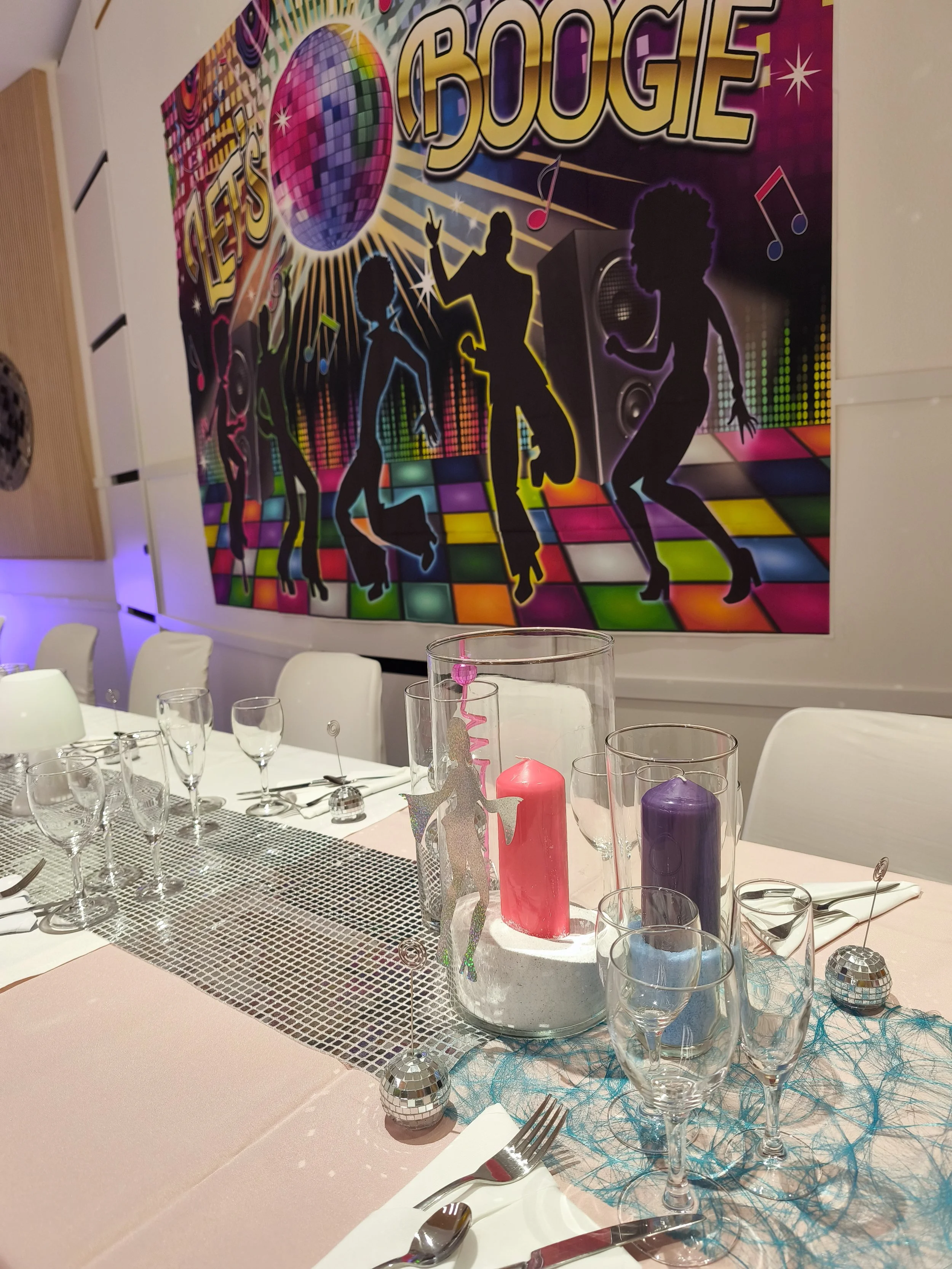 Décoration pour une fête avec une affiche de disco avec un ballon miroir, silhouettes de danseurs, et des imprimés de notes de musique. La table est ornée de bougies colorées, de décorations disco et de verres à vin.