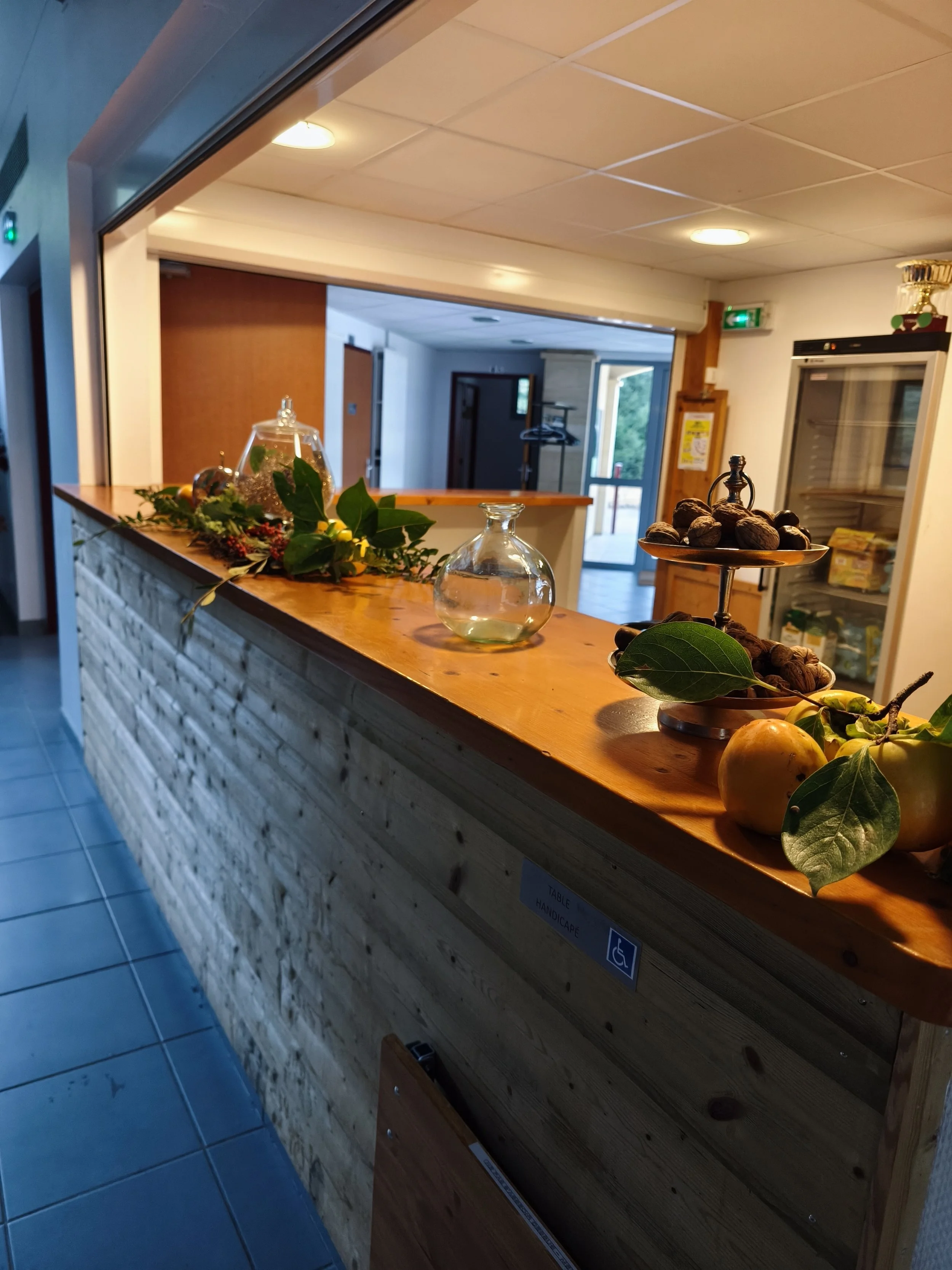 Un comptoir en bois avec des décorations de noix, de fruits et de feuillage, dans une salle intérieure d'un bâtiment, avec une porte et un frigo en arrière-plan.