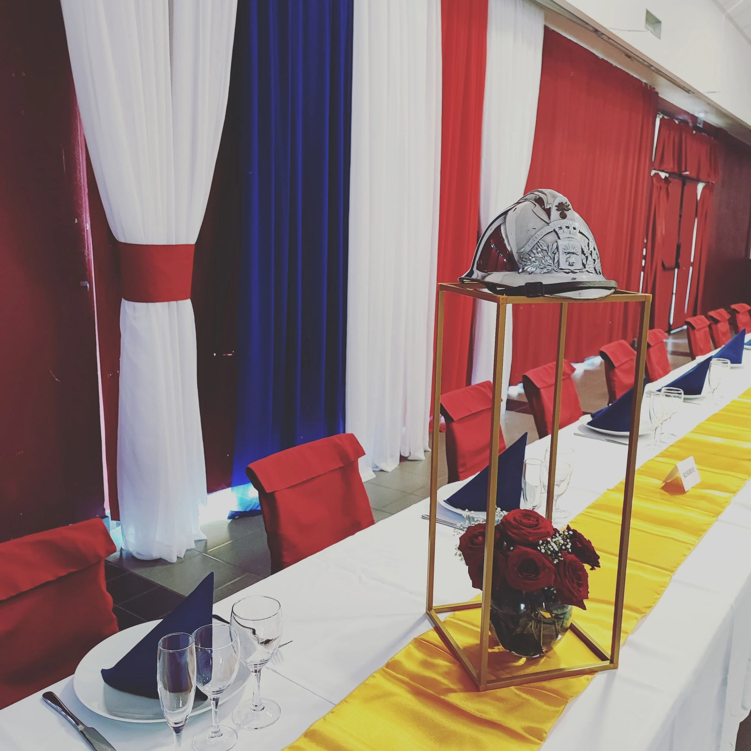 Décorations de fête de style patriotique avec beaucoup de draperies rouge, blanc, bleu, une table avec des verres à champagne, une nappe jaune et un casque d'officier ou militaire posé sur une petite table.