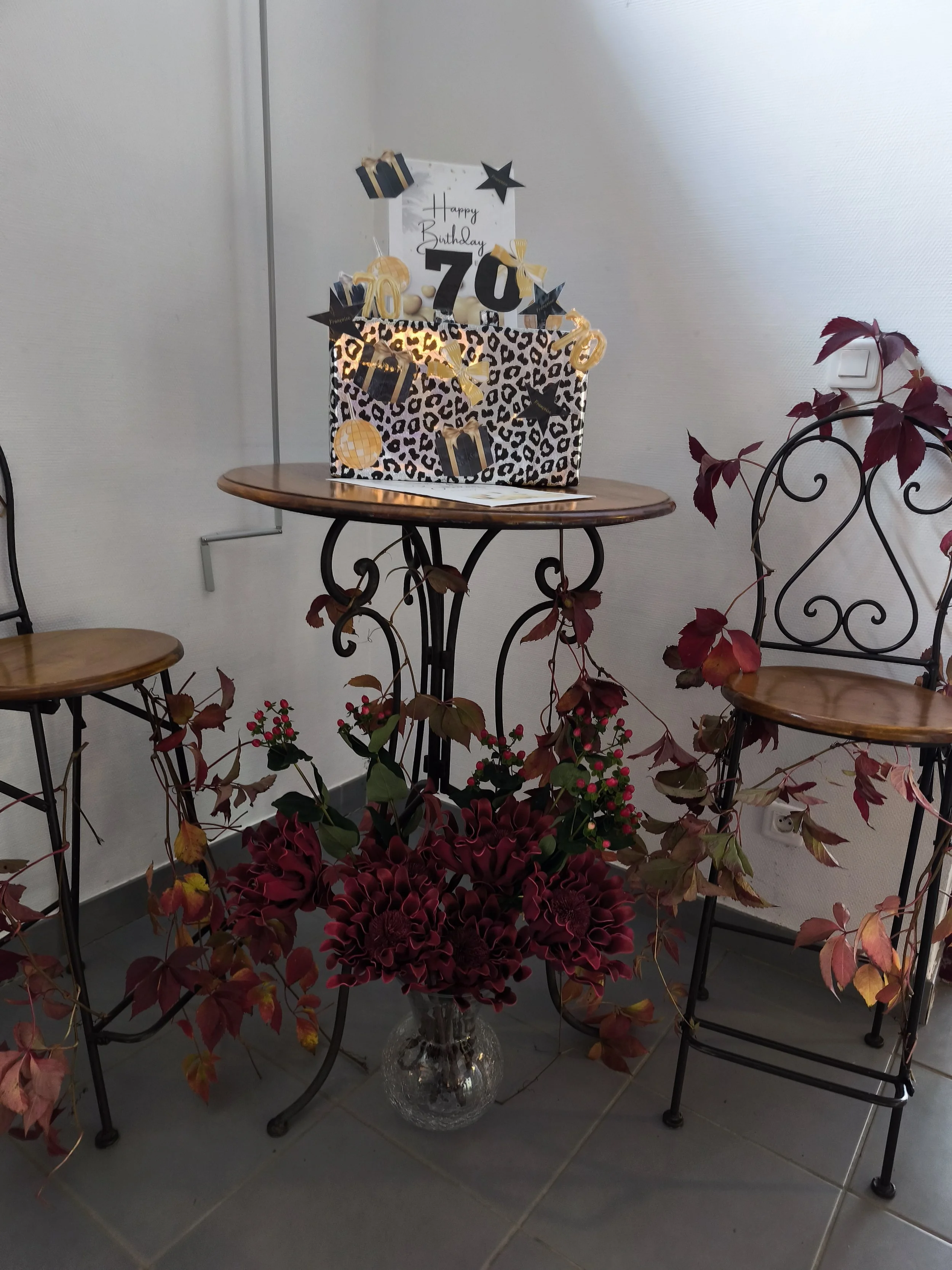Une décoration d'anniversaire pour une personne fêtant ses 70 ans, comprenant un cadeau, des ballons, des rubans, des étoiles et des chiffres 70, avec des fleurs et des feuillages devant.