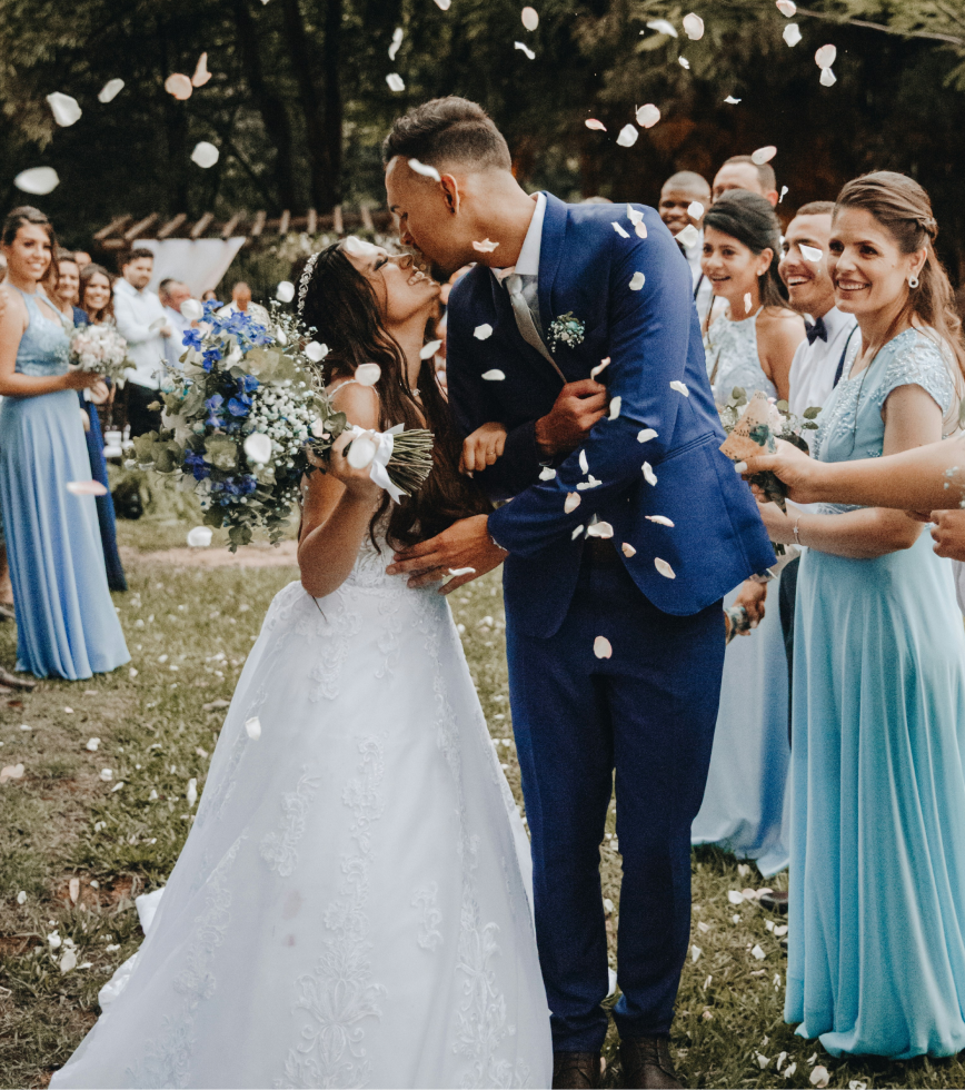 Un couple de mariés s'embrassent lors de leur mariage en plein air, entourés d'amis et de famille qui fête, avec des confettis dans l'air.