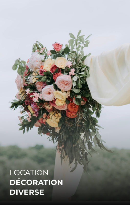 Un bouquet de fleurs colorées, avec des roses de différentes couleurs, tenu par une personne portant une robe blanche, avec un fond naturel flou.