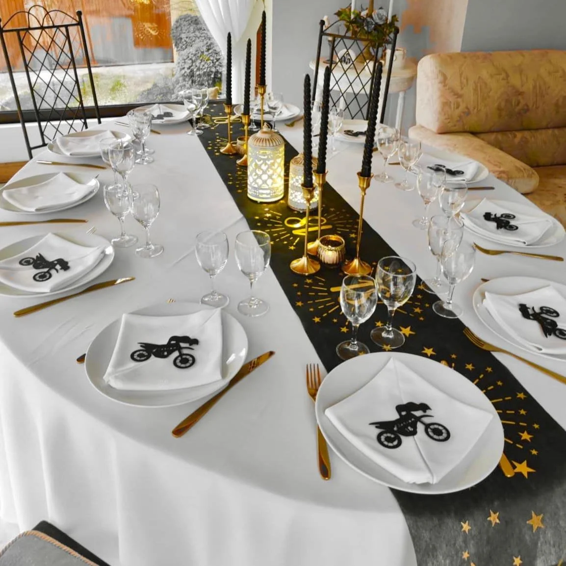 Table de fête avec nappe blanche, décoration noire et dorée, bougies, et assiettes avec serviettes dessus affichant une moto noire.
