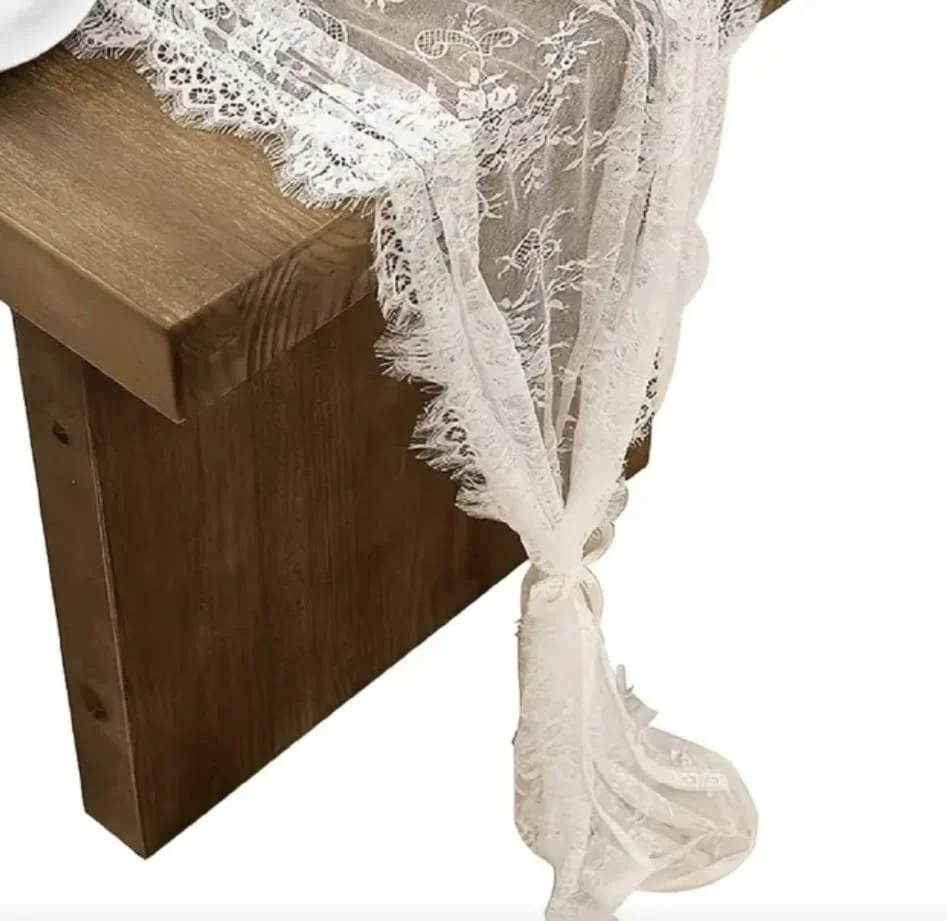 Un tissu en dentelle blanche est attaché à une table en bois, formant un nœud, avec un motif floral et une bordure en crochet.