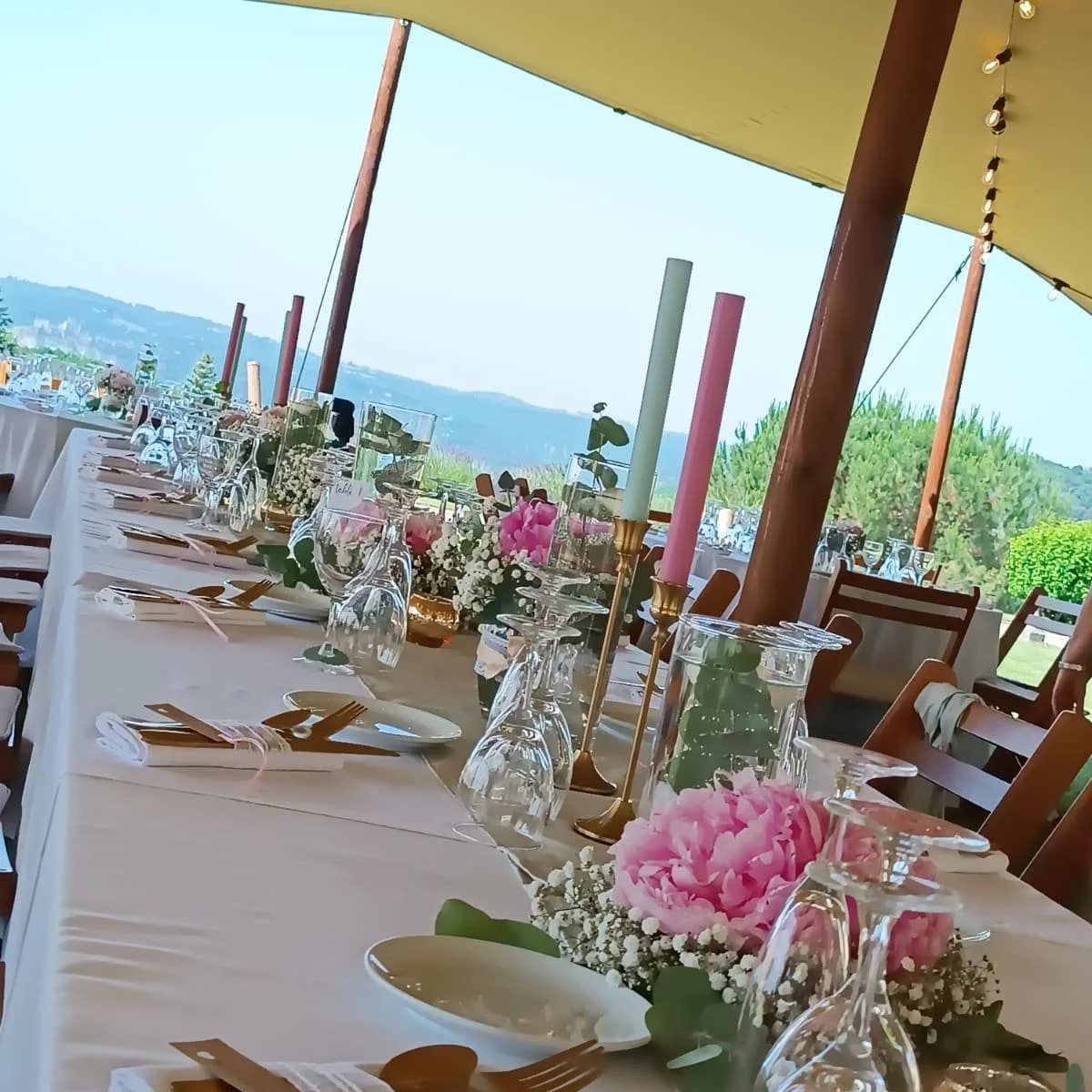 Table de mariage décorée avec fleurs, bougies et vaisselle élégante dans un lieu en plein air avec vue sur la nature.