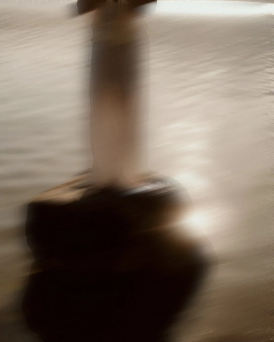 Blurred photo of a person walking on a concrete surface, with a focus on their legs and shoes.