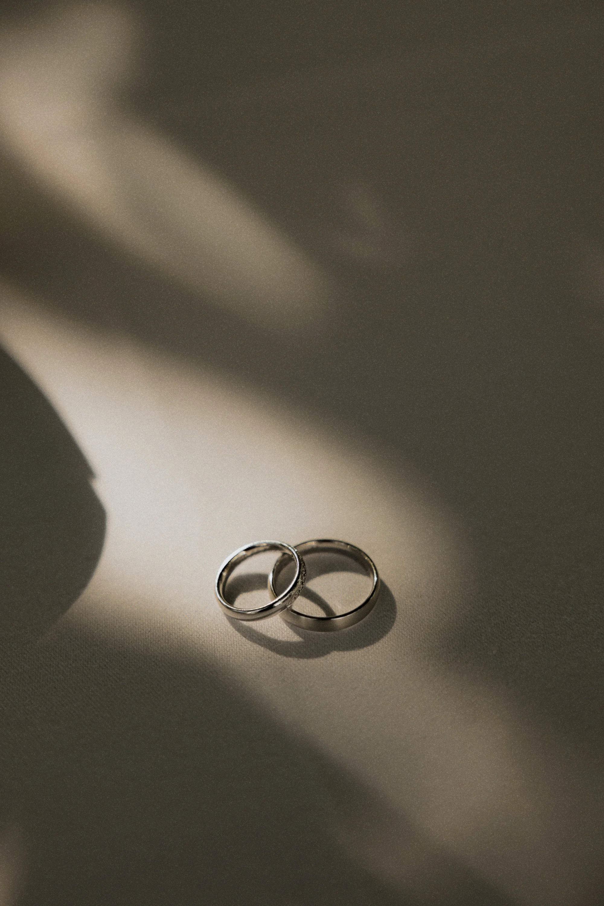 Close-up of two wedding rings, one slightly overlapping the other, on a grey surface with shadows.