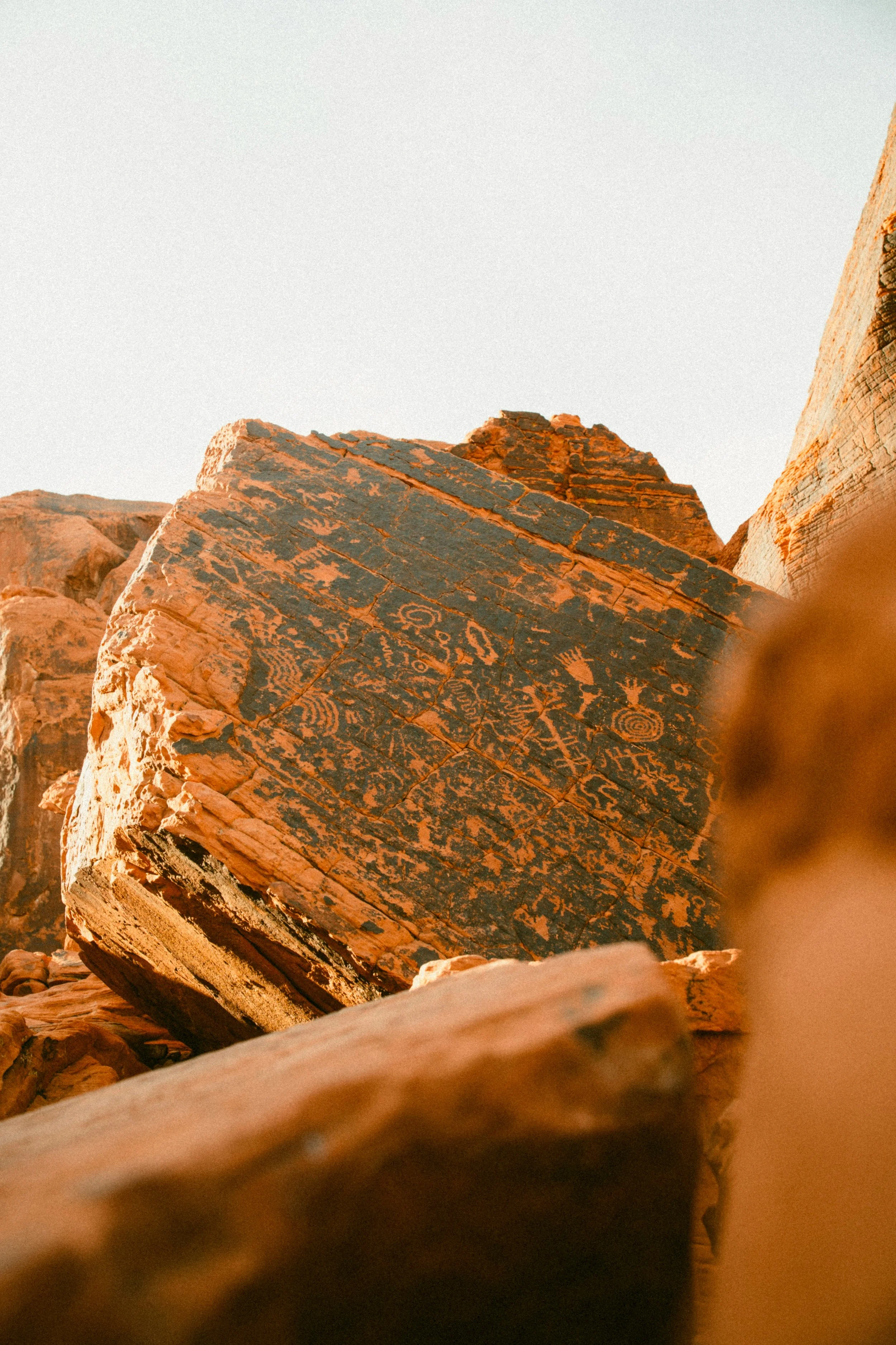 Close-up of large, weathered rocks in a desert landscape, with petroglyph carvings visible on one rock surface at sunset or sunrise.