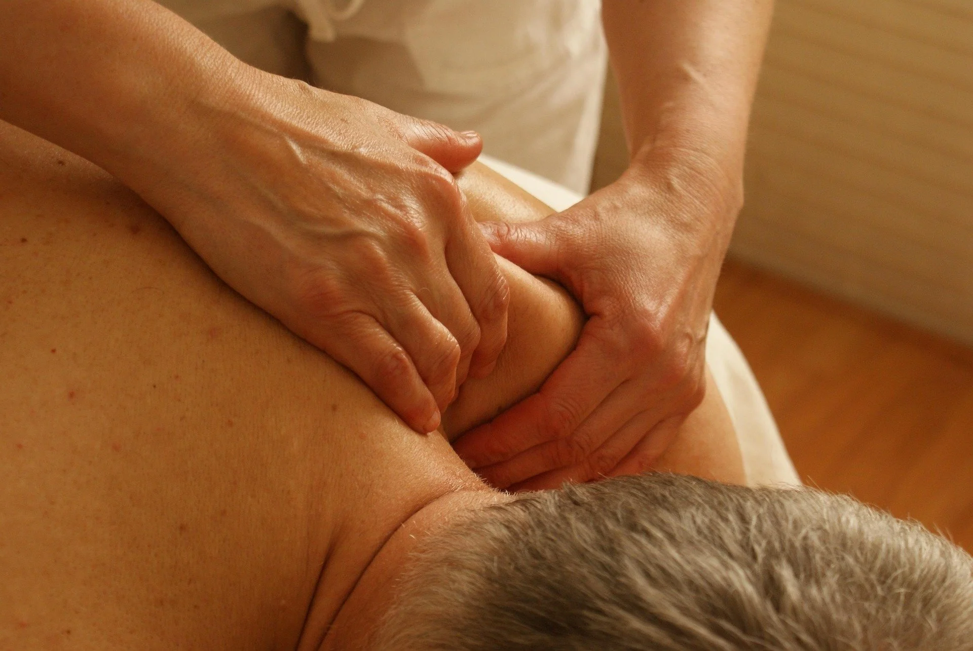 A person receiving a massage, lying face down with hands applying pressure on their back.