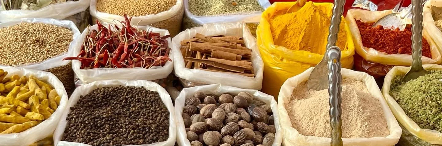 Spice market with various spices and herbs in open bags, including red chili peppers, turmeric, cinnamon sticks, dried herbs, and peppercorns.
