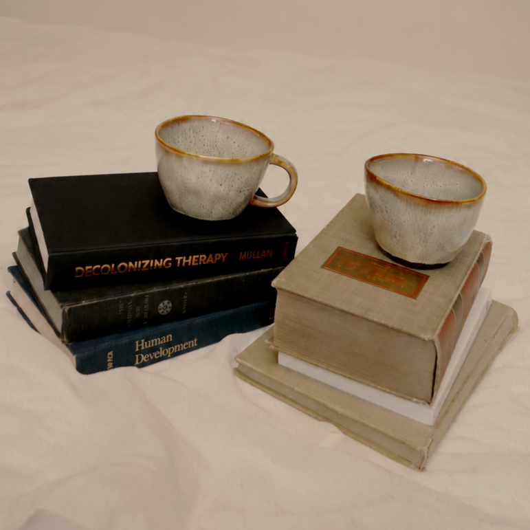 Two ceramic cups placed on stacks of four books each, with the cups on the left on a black stack and the cups on the right on a beige stack, all set against a white background.
