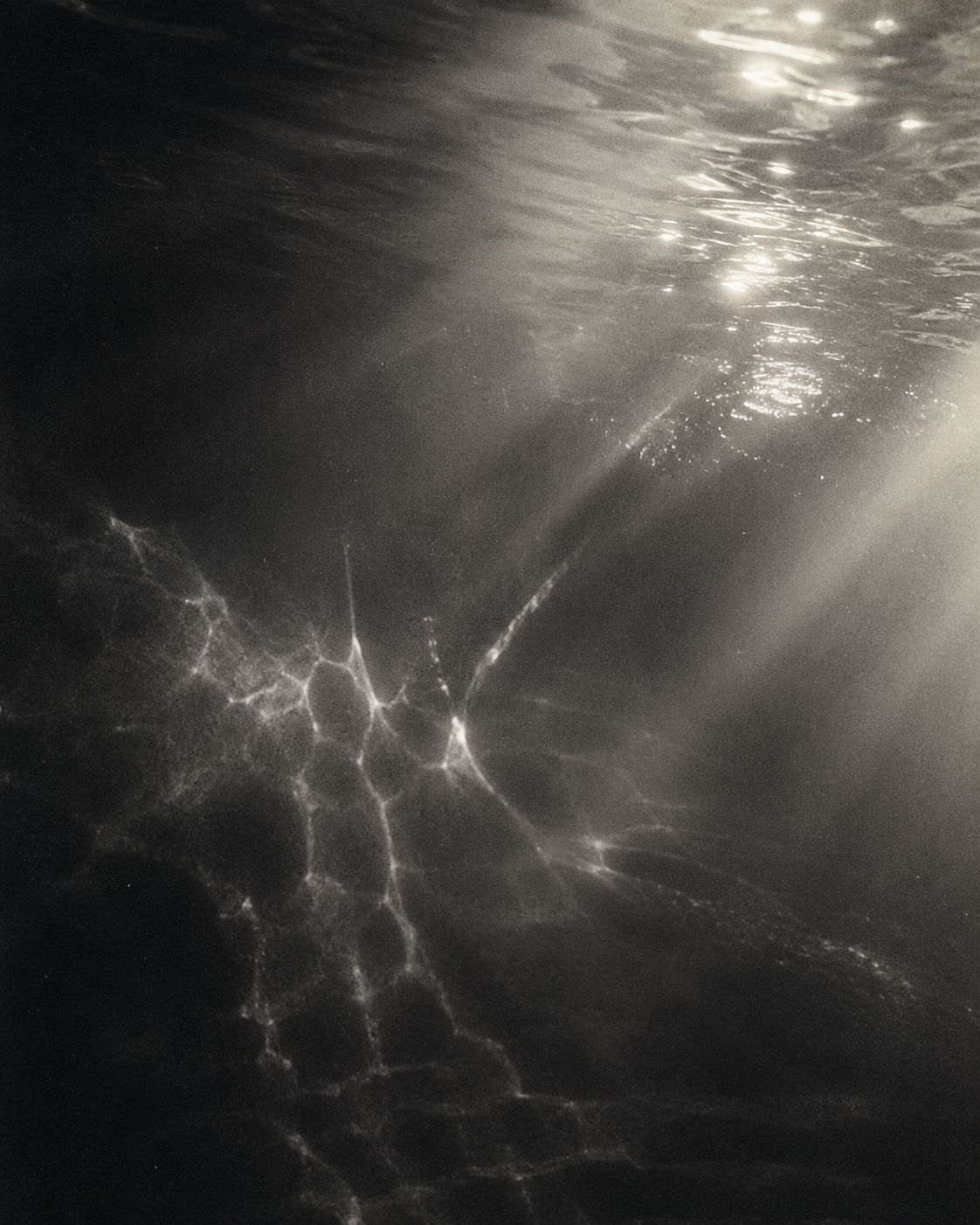 Underwater scene with light reflections on the ocean floor and surface.