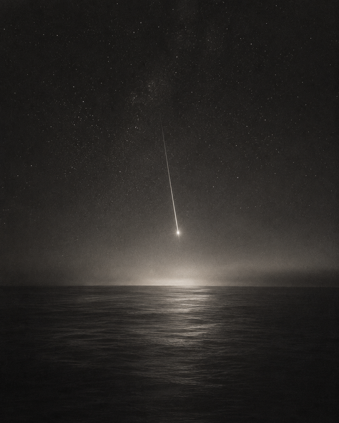 A night sky over the ocean, with numerous stars and a bright meteor streaking across the sky.
