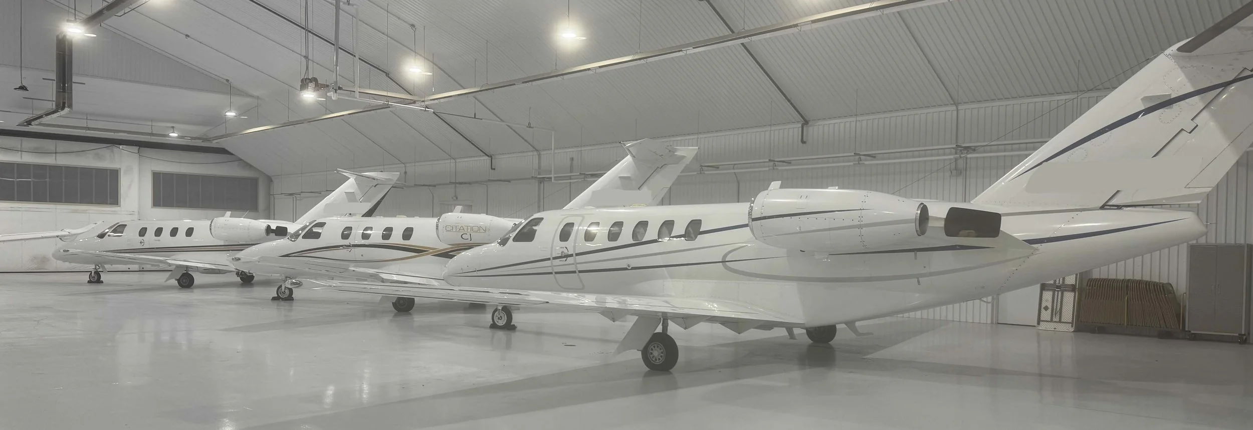 Three private jets parked inside an aircraft hangar with a white interior and high ceiling. Fleet Support.