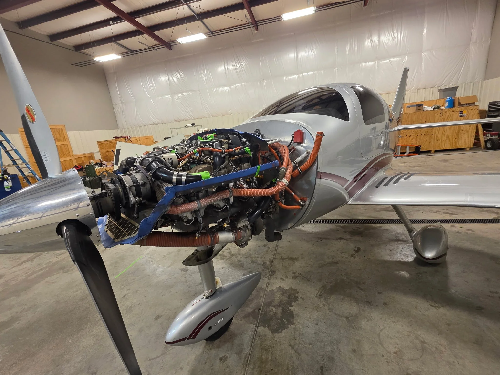 An aircraft fuselage inside a workshop, with the engine and internal components exposed. Columbia 400.