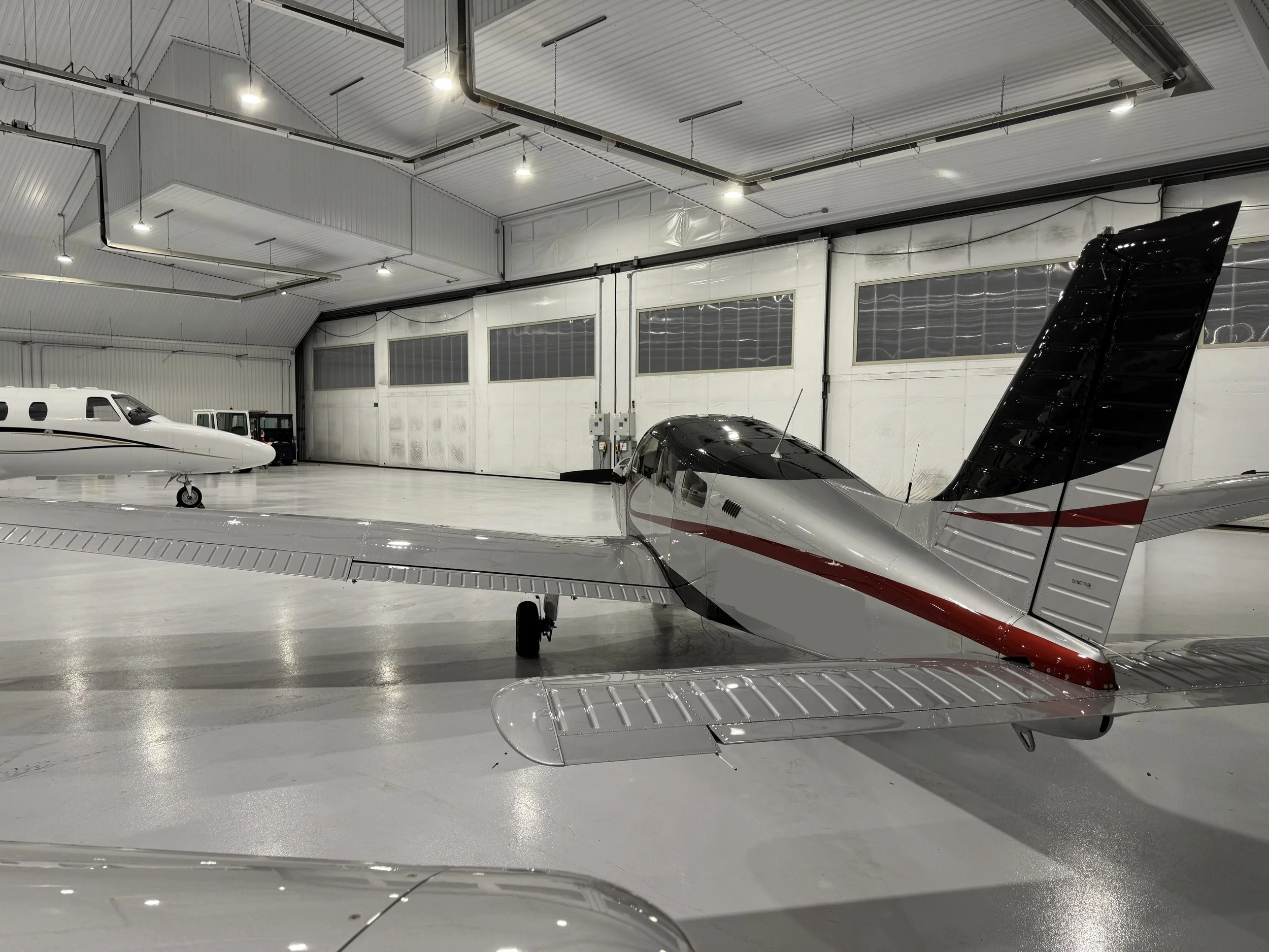 Interior of an aircraft hangar with airplanes parked inside, white walls, and bright overhead lighting. Detailing on new Piper PA-28, Archer.