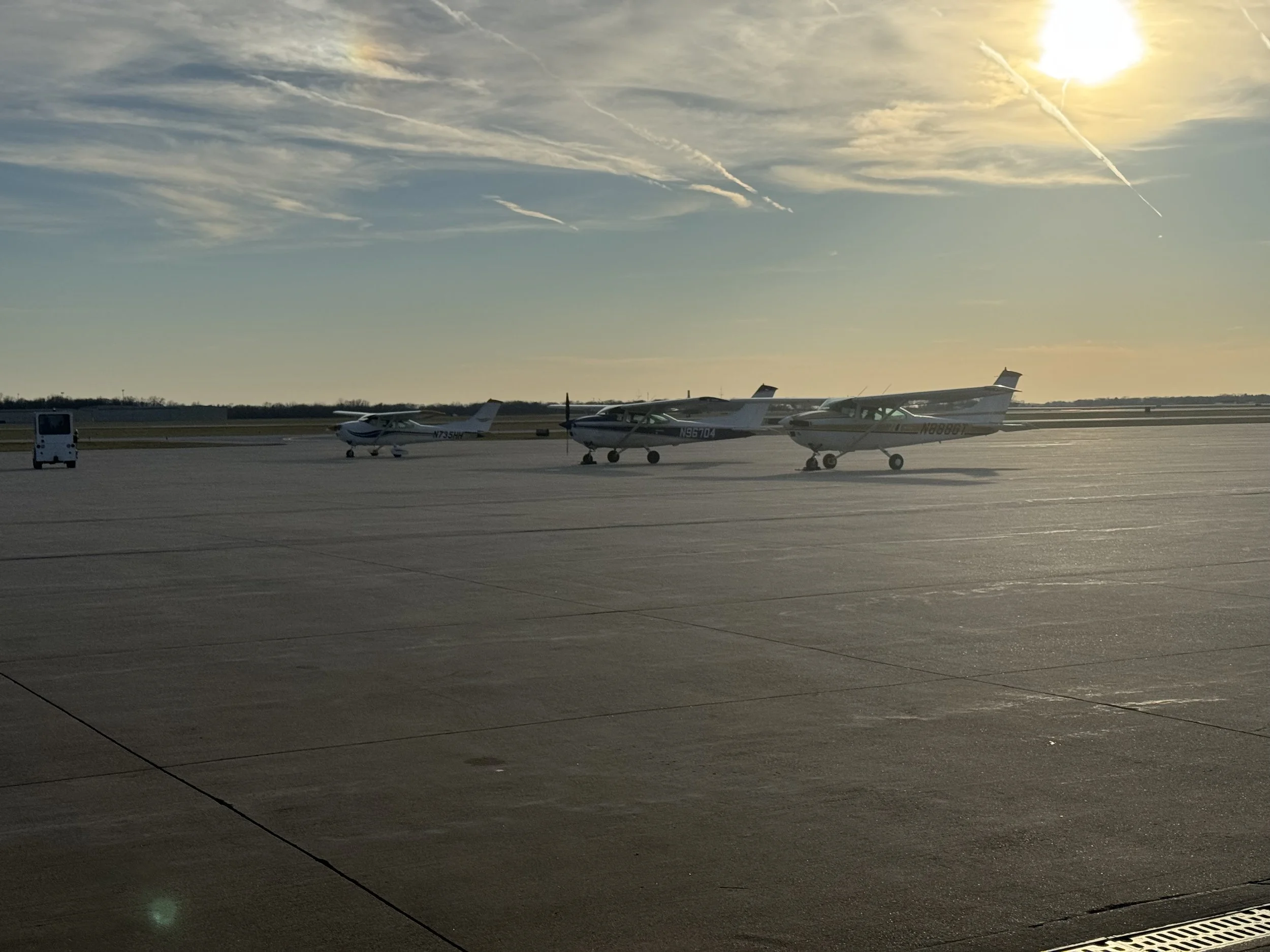 Three small private airplanes parked on an airport tarmac during sunset with a bright sun and partly cloudy sky. Fleet Support.