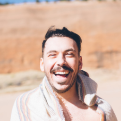 Billy Gaffney smiling outdoors with a rocky background, wearing a light-colored scarf