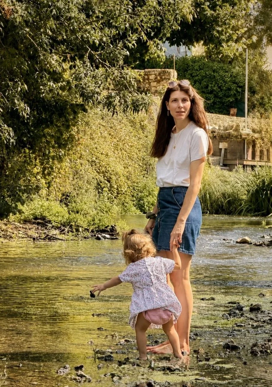 Une femme et un jeune enfant jouent dans une rivière aux côtés de végétation abondante, en plein air.