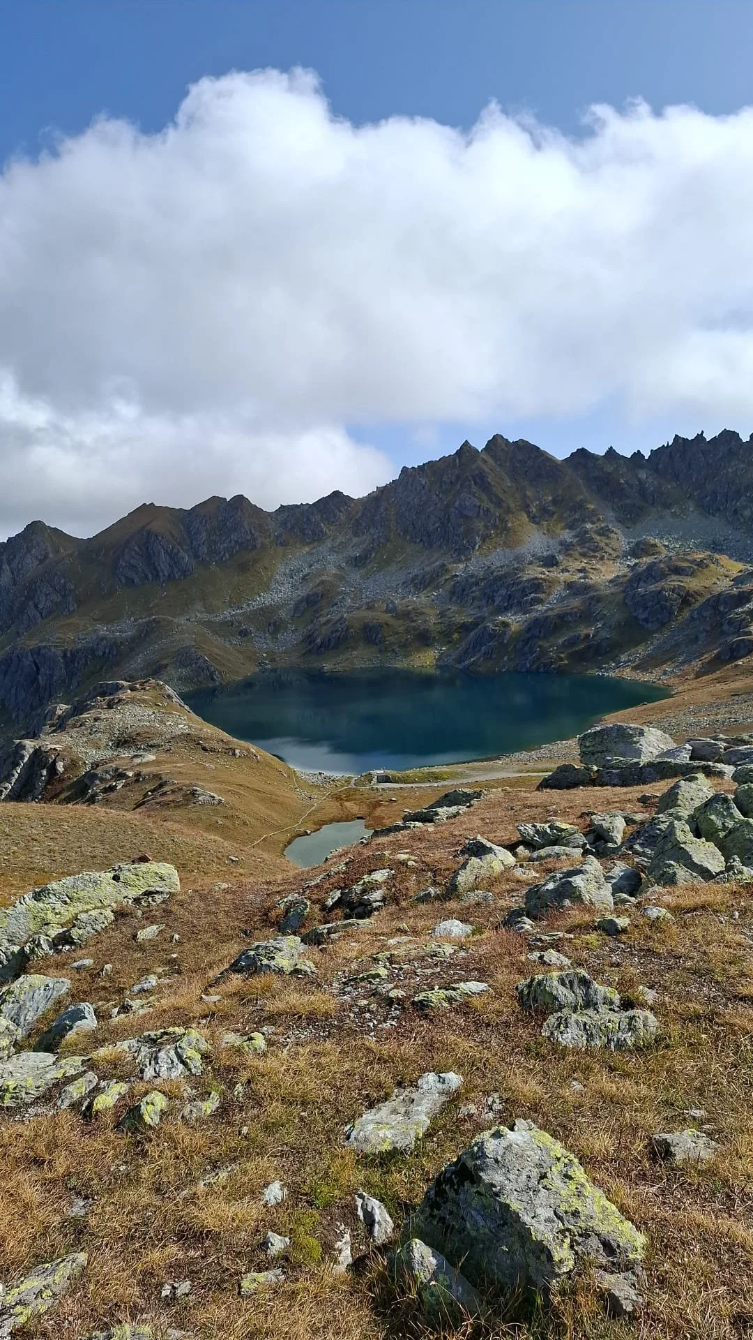 Paysage de montagne avec deux lacs, rochers et herbe, ciel partiellement nuageux.