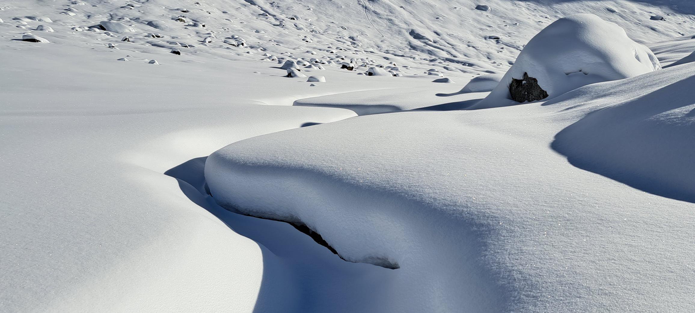 Paysage enneigé avec des rochers recouverts de neige et des formations de neige sculptées par le vent sous un ciel clair.