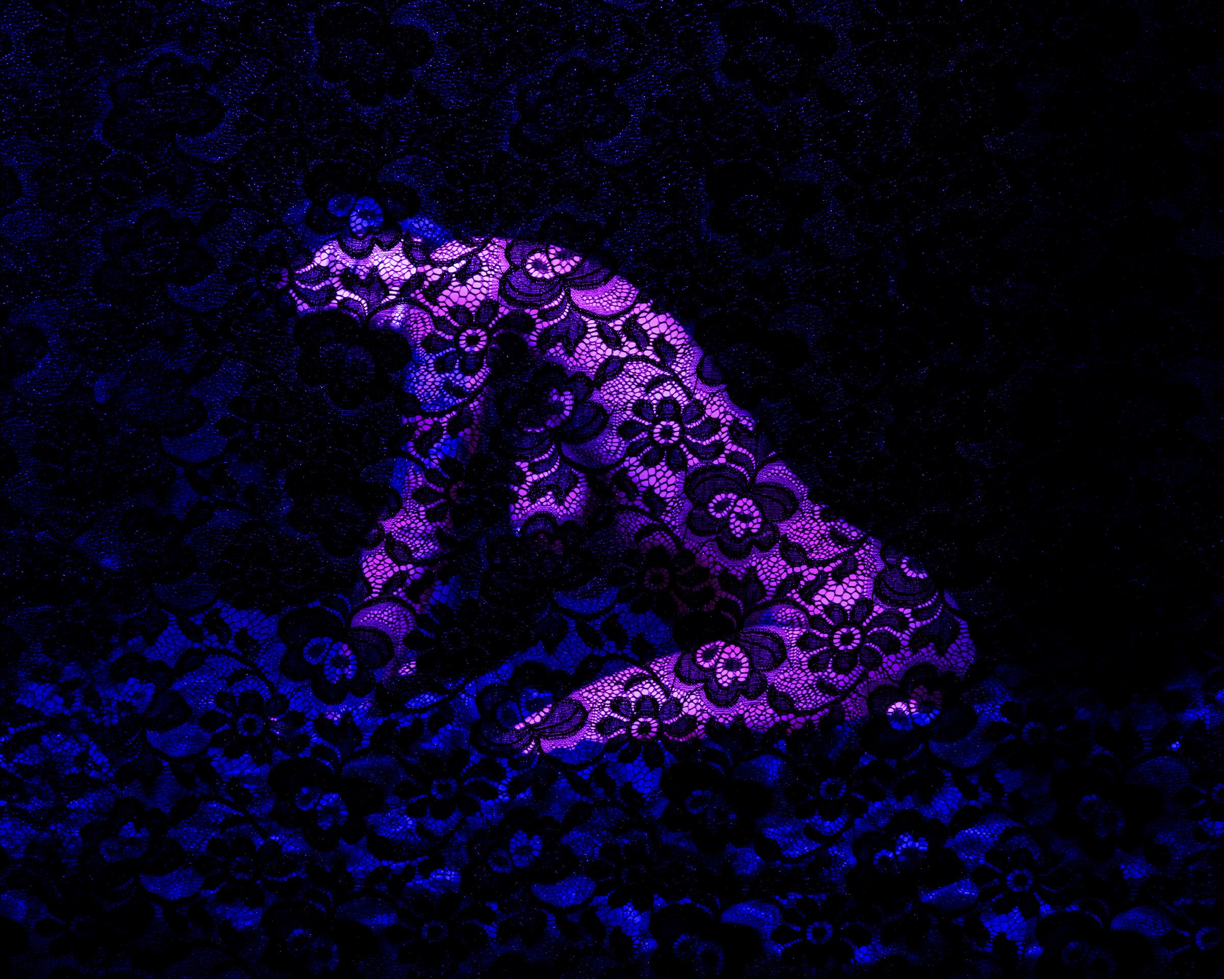 Close-up of a lace fabric with black and purple floral patterns illuminated under blacklight.